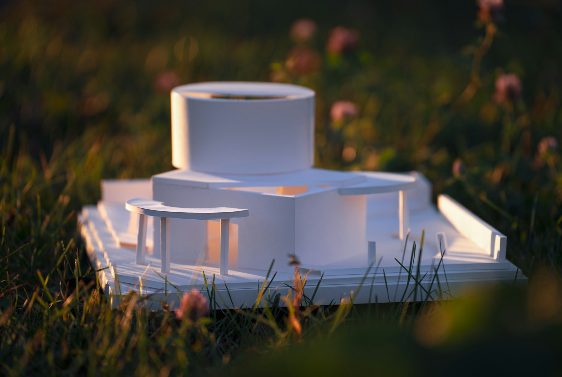 White card architectural model placed in a meadow at golden hour