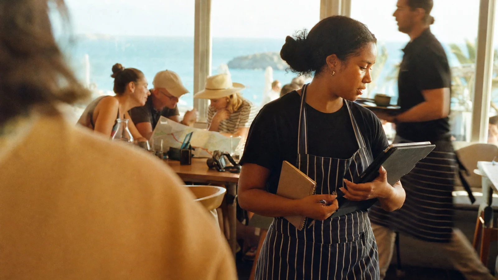 Cameriera cambia la lingua del menu sul tablet tra i tavoli di un ristorante sul mare