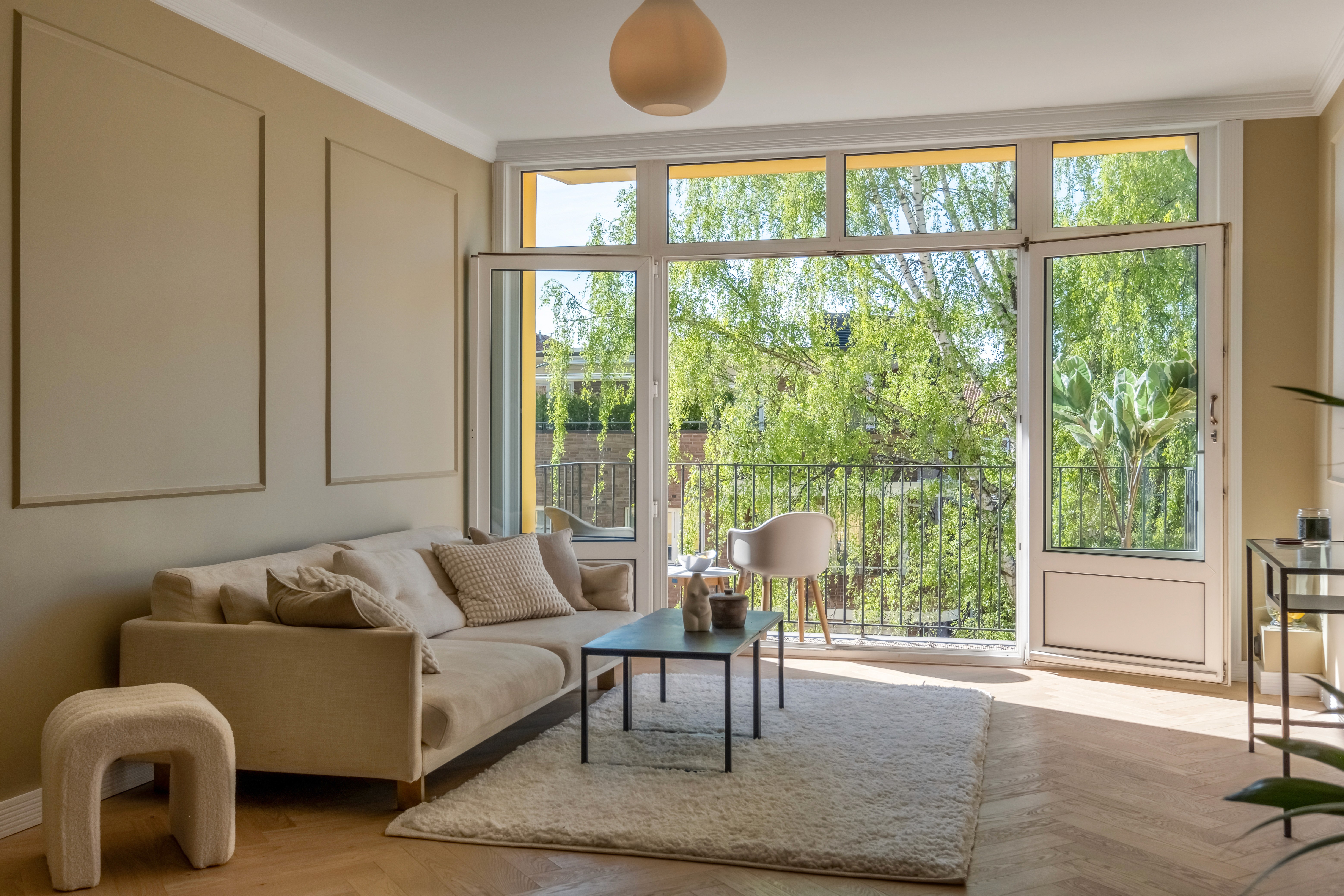 Stue med beige sofa, store vinduer og utgang til balkong