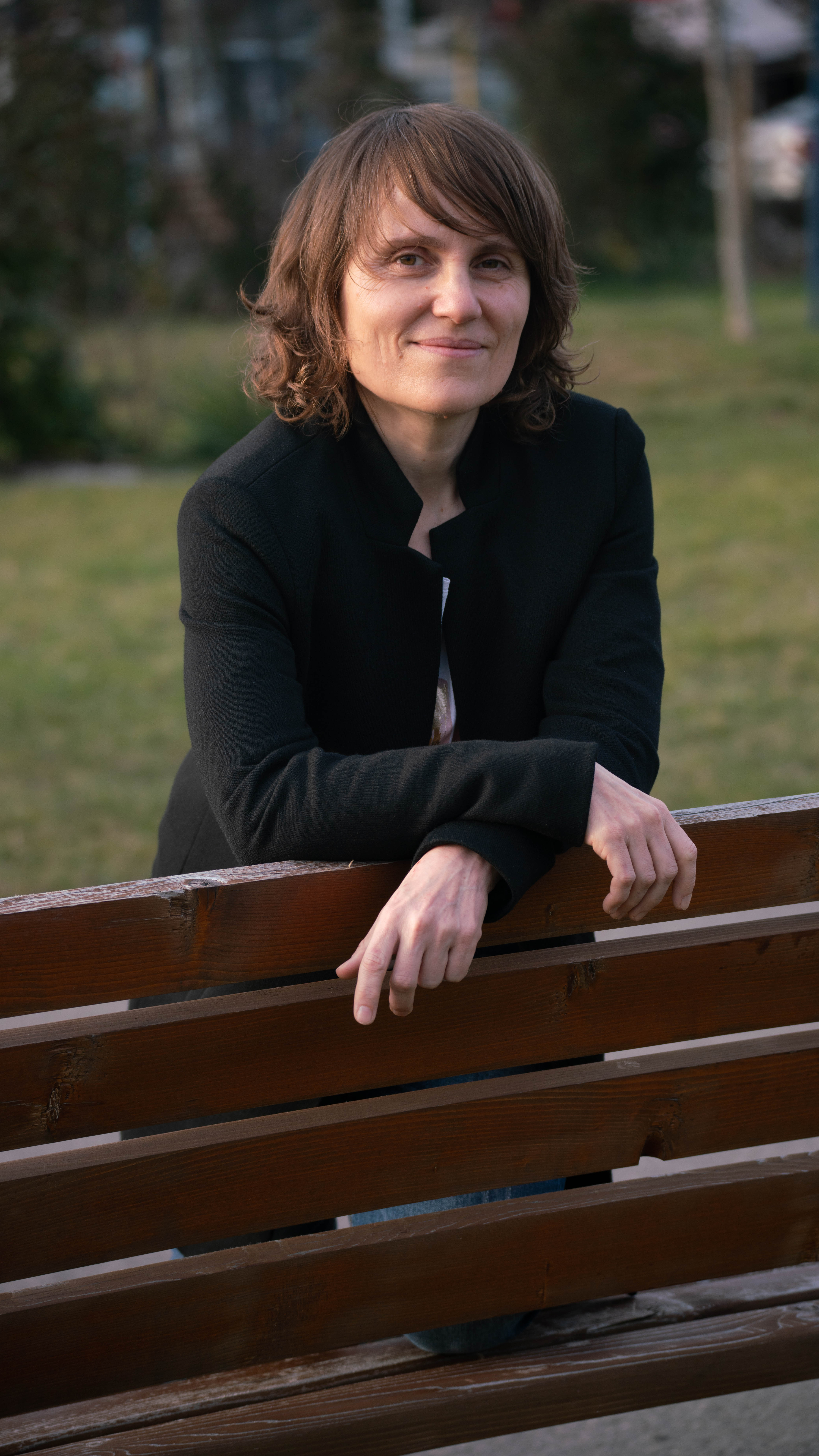 Adriana Georgescu, executive coach, leaning on a wooden bench outdoors with a relaxed smile.