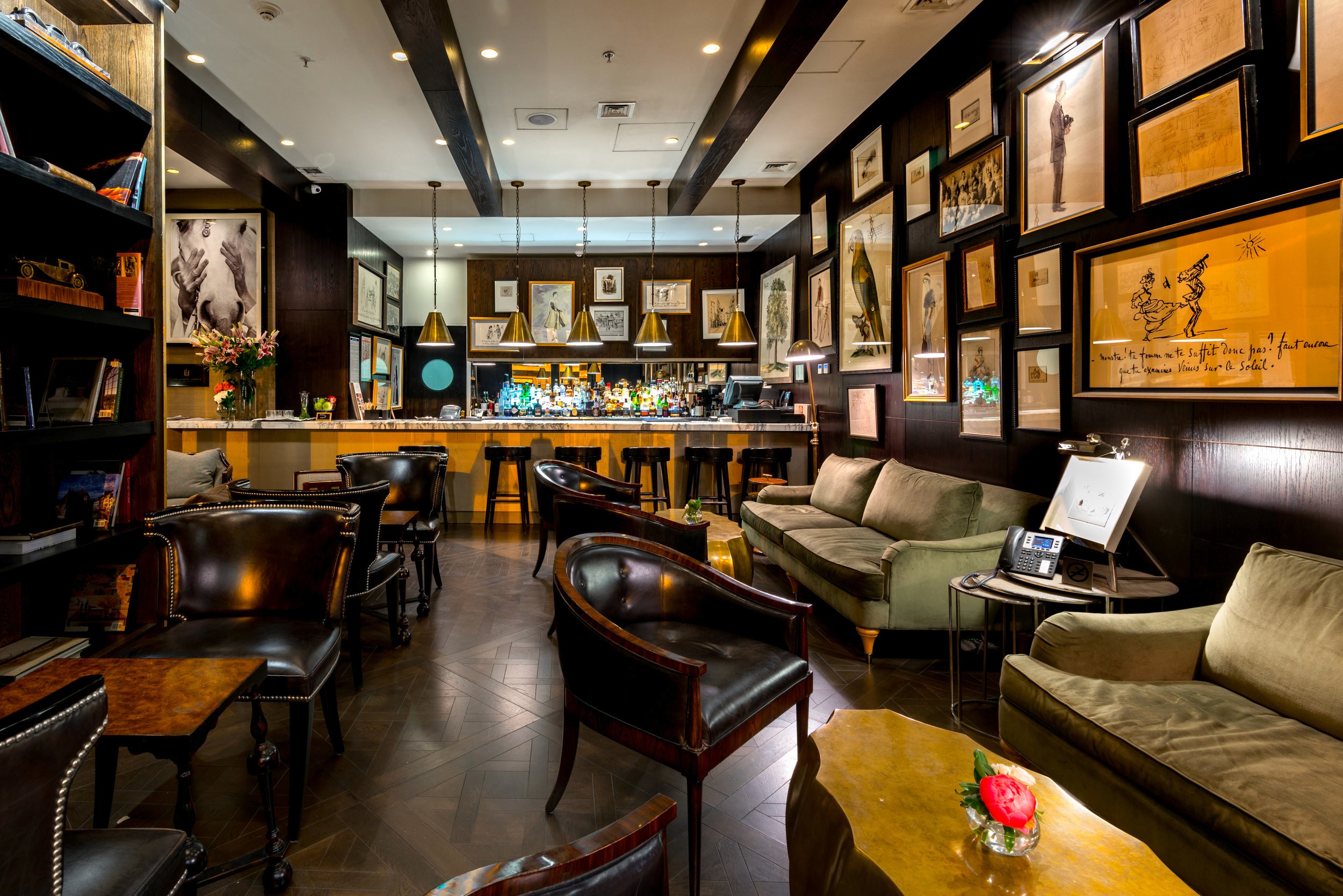 A dimly lit pub interior with leather chairs, a long wooden bar, and framed photos on walls under warm hanging lights.