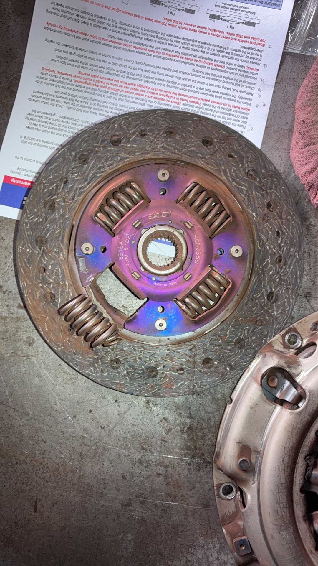 Used Exedy clutch disc on a shop bench with one damper spring out of its window and the plate around it broken away