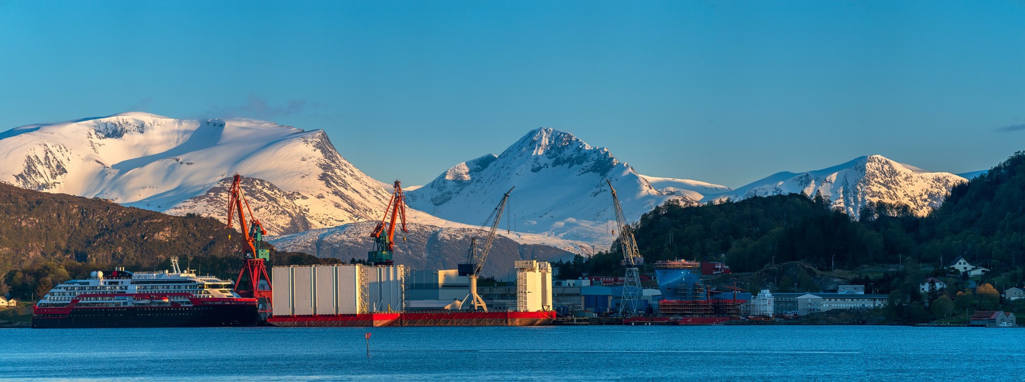 Snow-capped mountains rise over a calm blue lake under a clear sky, reflecting the scenery.
