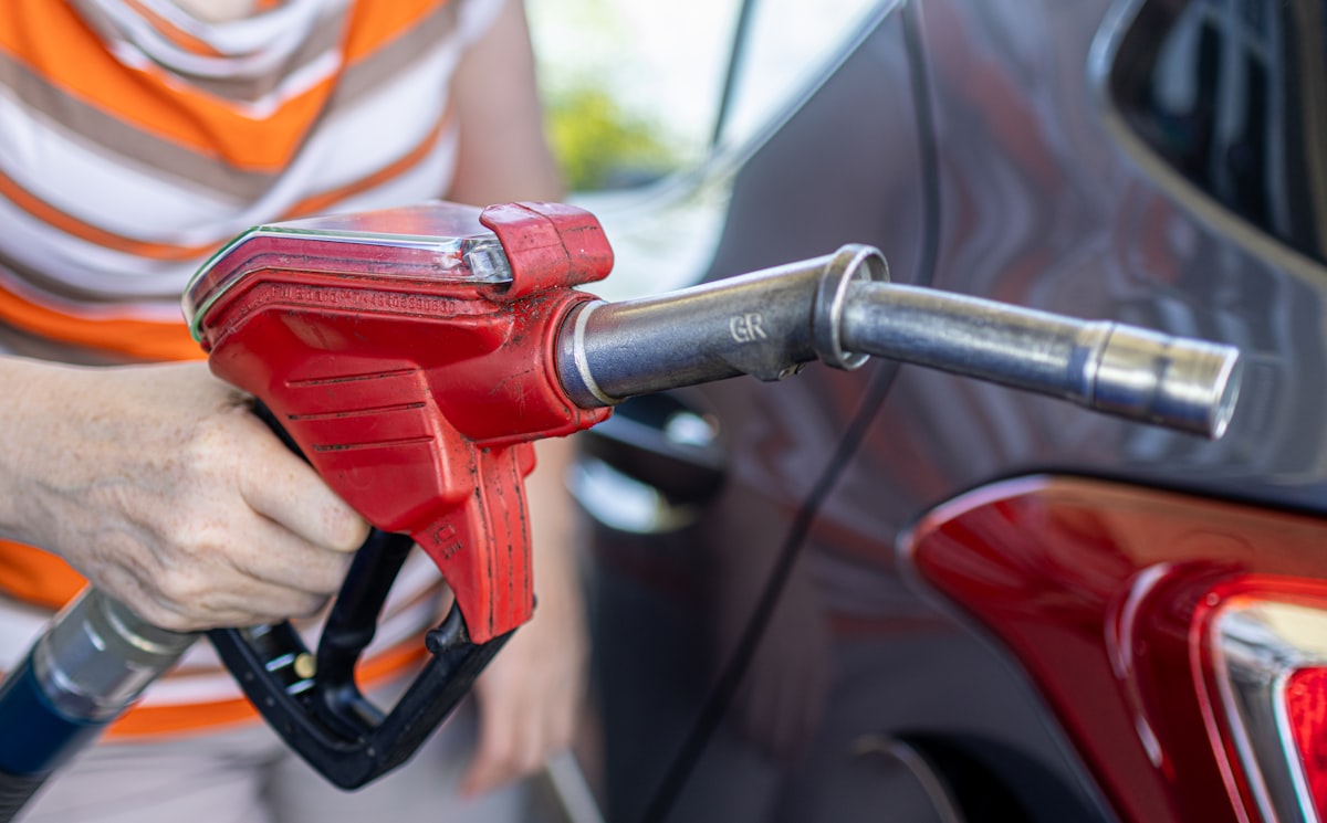 Woman refueling a car at a gas station pump, where the drive or fly cost math starts