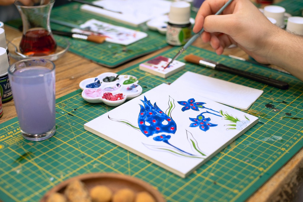 Workspace with a participant painting blue floral patterns during a Turkish tile workshop in Istanbul. This ceramic art workshop is a top recommendation for what to do in Istanbul.