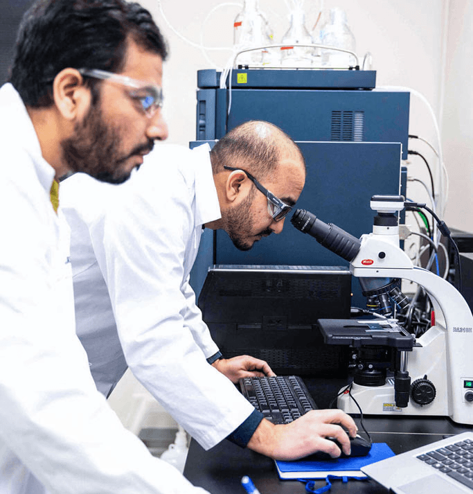 SteriMax scientists examining a sample under a microscope while a colleague records notes in a laboratory.