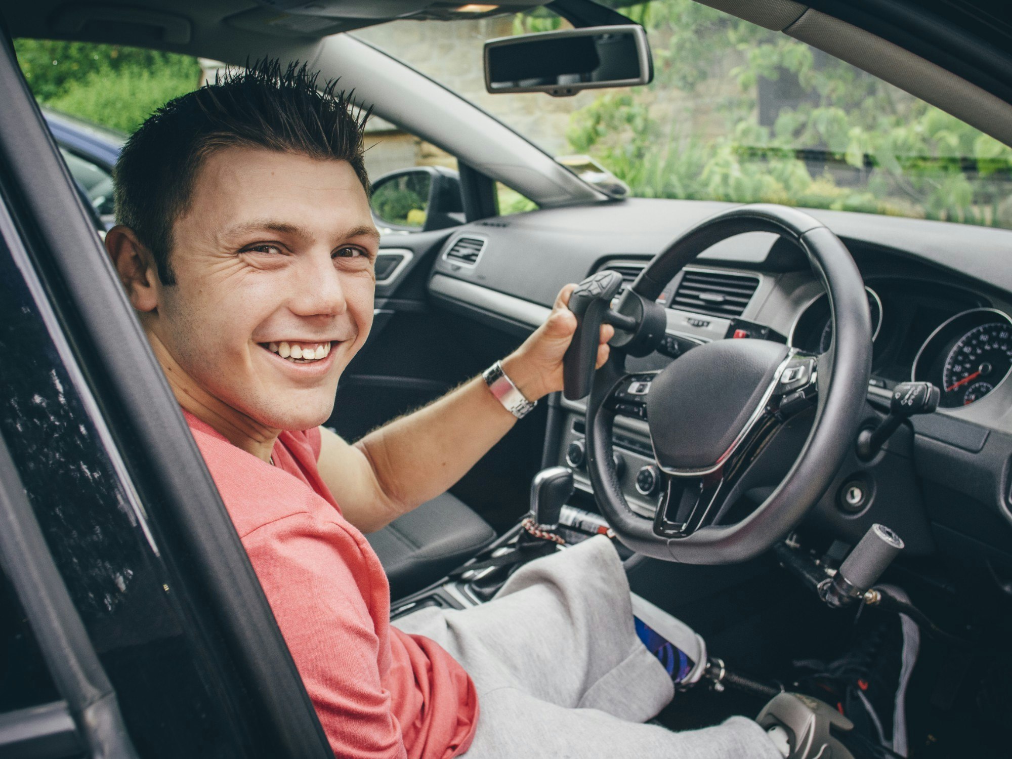 Male seated in the driver seat of a vehicle fitted with modified steering controls for driving.