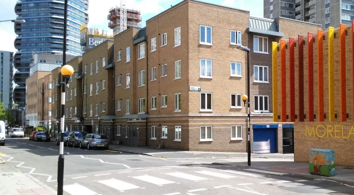 Modern arch-shaped building with glass facade reflects in an infinity pool at sunset. A silhouetted palm tree adds to the serene, elegant scene.