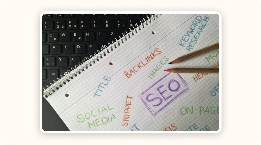 A handwritten SEO plan on graph paper showing backlinks, keyword research, titles, social media, and on-page SEO — placed on a laptop keyboard.