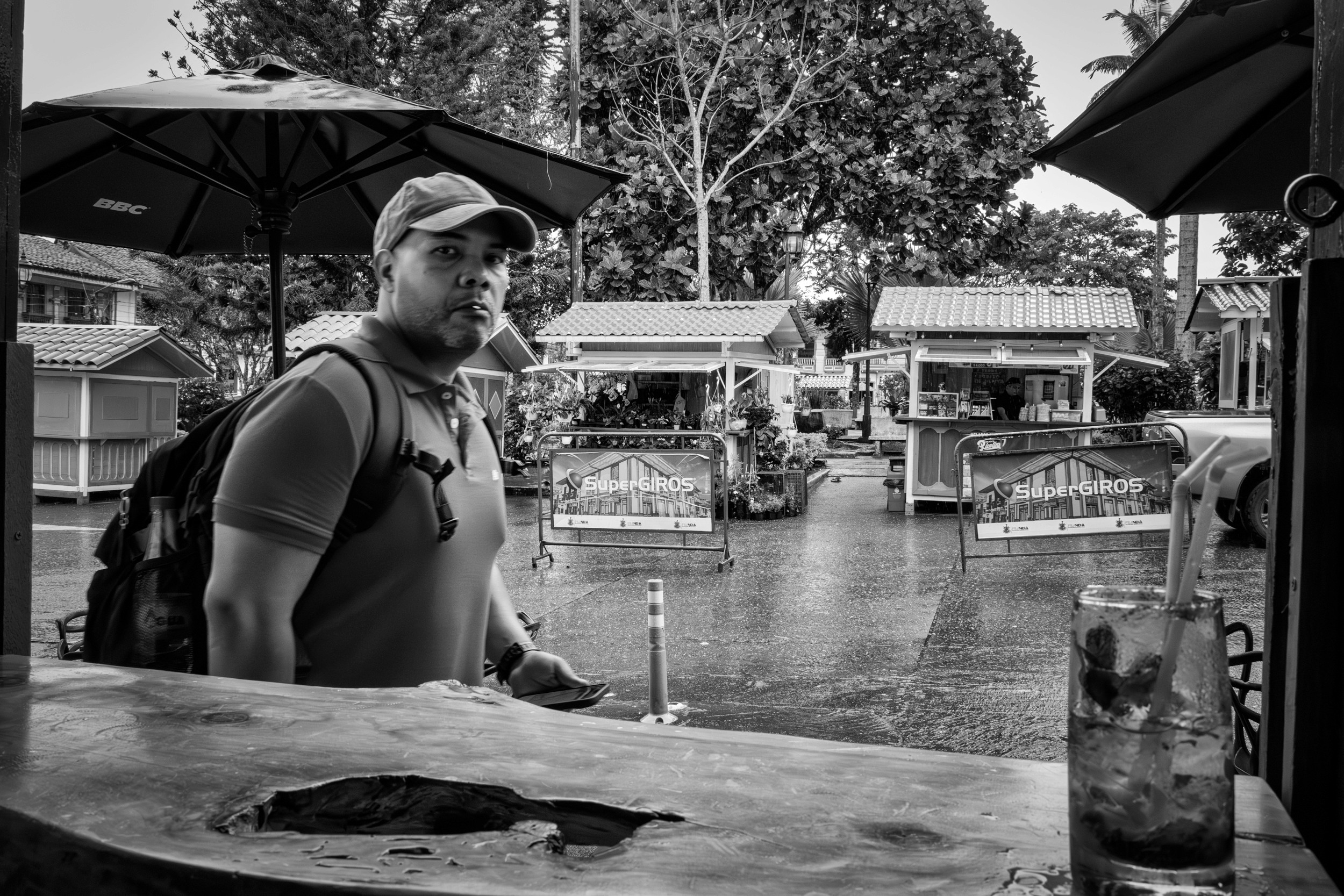 Rainy street scene with people passing by a bar window.