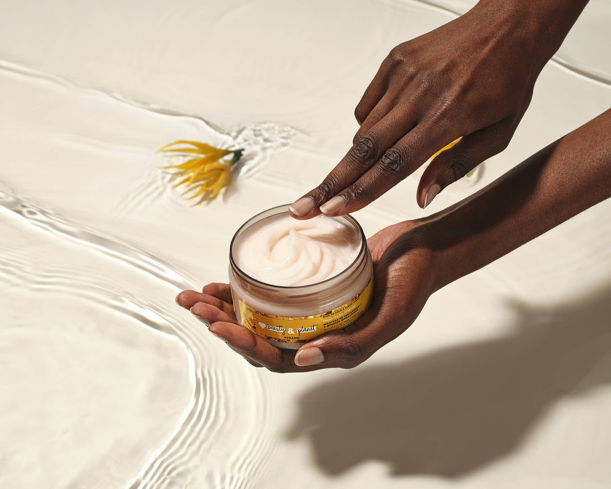 A person holds a small glass jar of cream, with a hand going to dip into the jar.