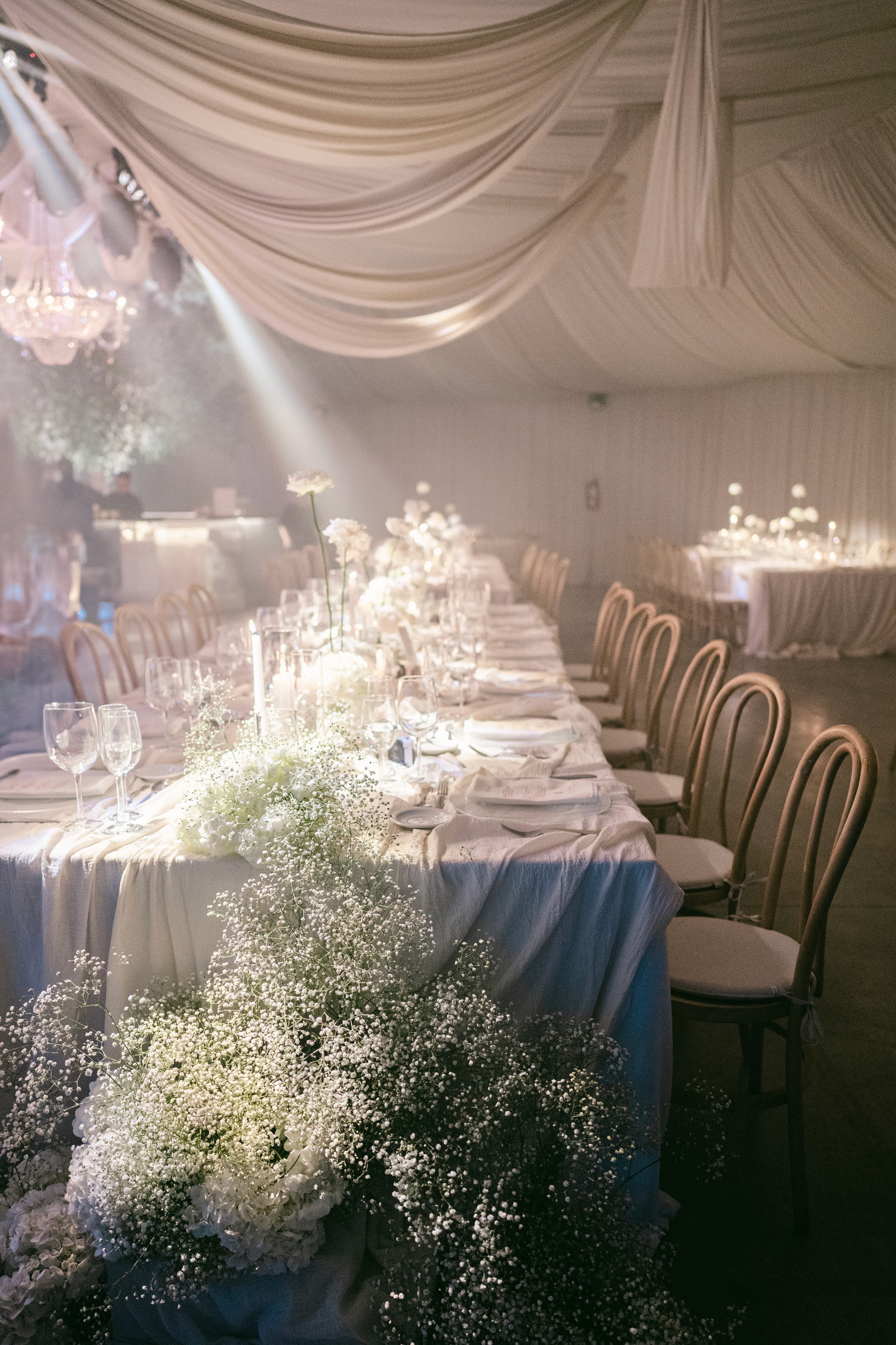 Puesta de mesa con cascada de gipsofila inmersiva, mantelería de lino y sillas Thonet de madera.