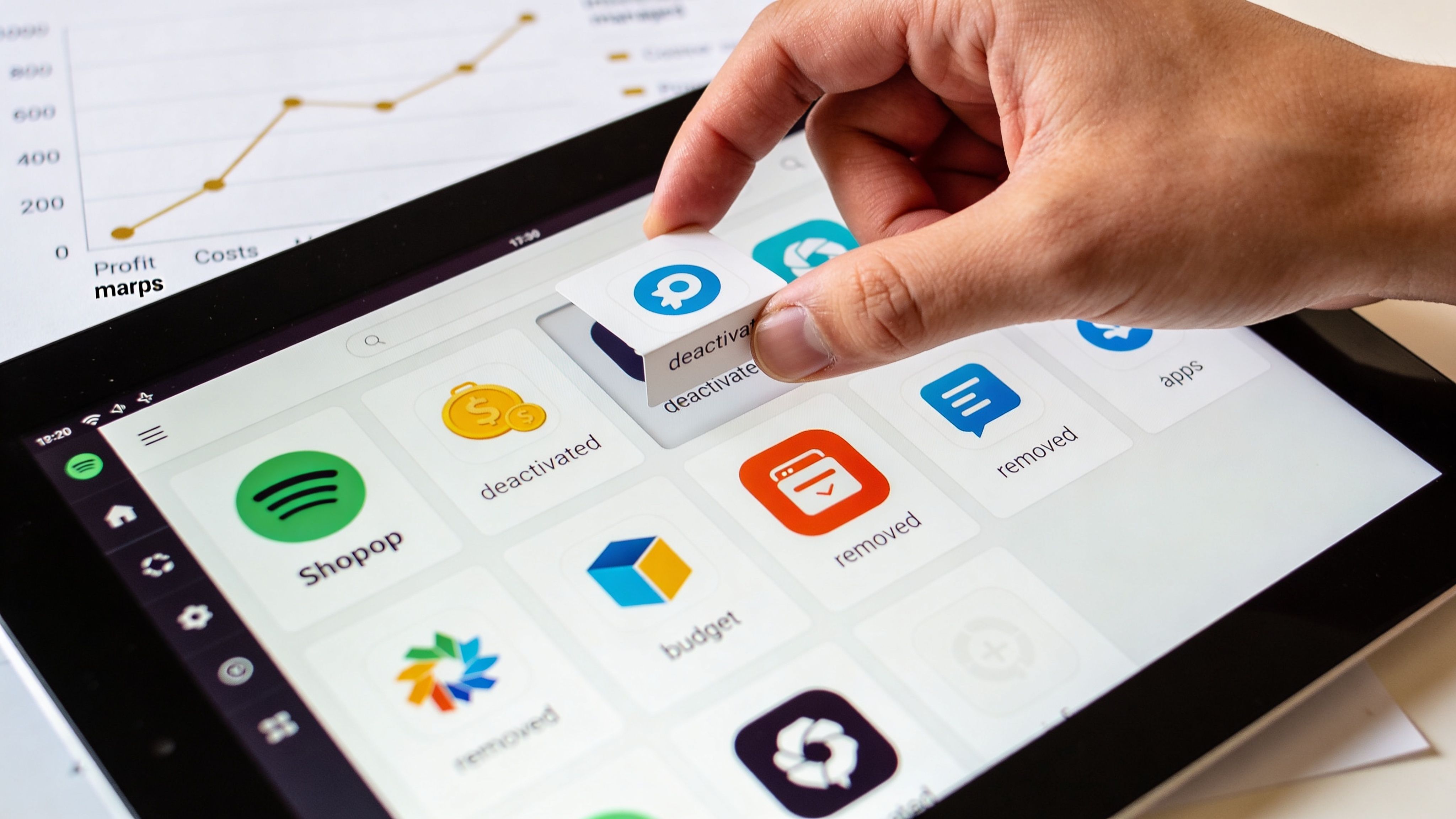 A hand placing an icon on a tablet screen displaying various application software and business interface elements.