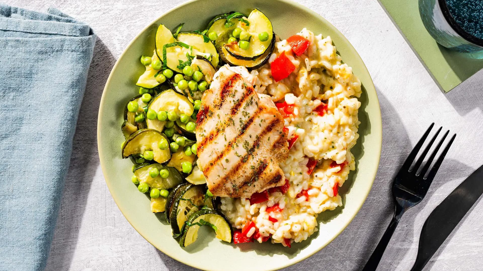 Hähnchenbrust mit cremigem Basilikum-Risotto, Zucchini und Gemüse auf einem Teller