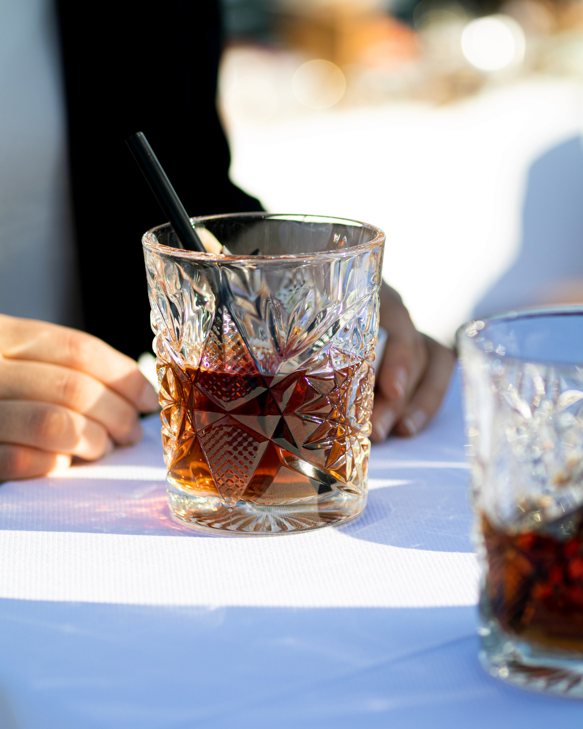 Gros plan ensoleillé sur un verre de whisky rempli à moitié avec une paille noir sur une table avec une nappe blanche