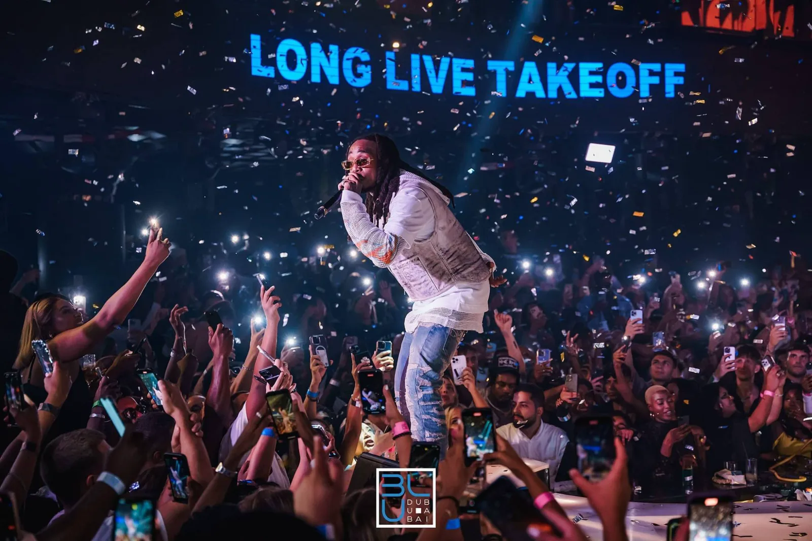 Rapper performing under a “Long Live Takeoff” screen as confetti falls over a crowd filming on their phones at BLU Dubai