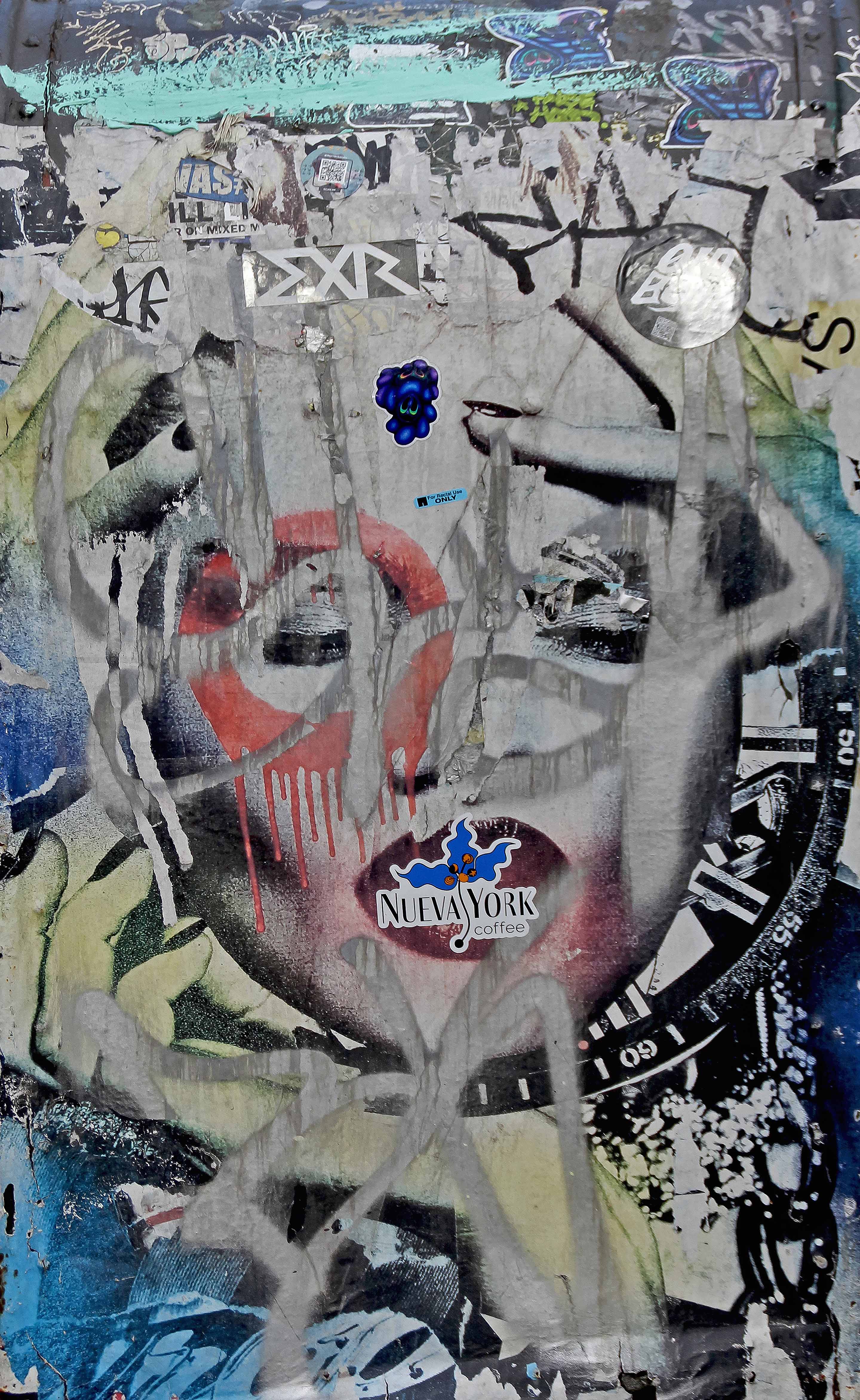 Photograph of a graffitied wall layered with spray paint, torn posters, and a partially obscured face. The overlapping marks and vivid colors merge into an expressive, chaotic portrait that captures the tension between creation and erasure.