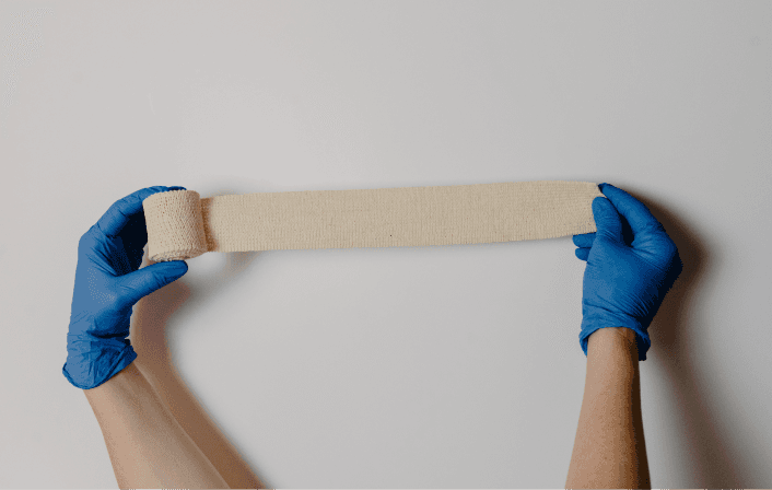 Hands in gloves holding a medical bandage.