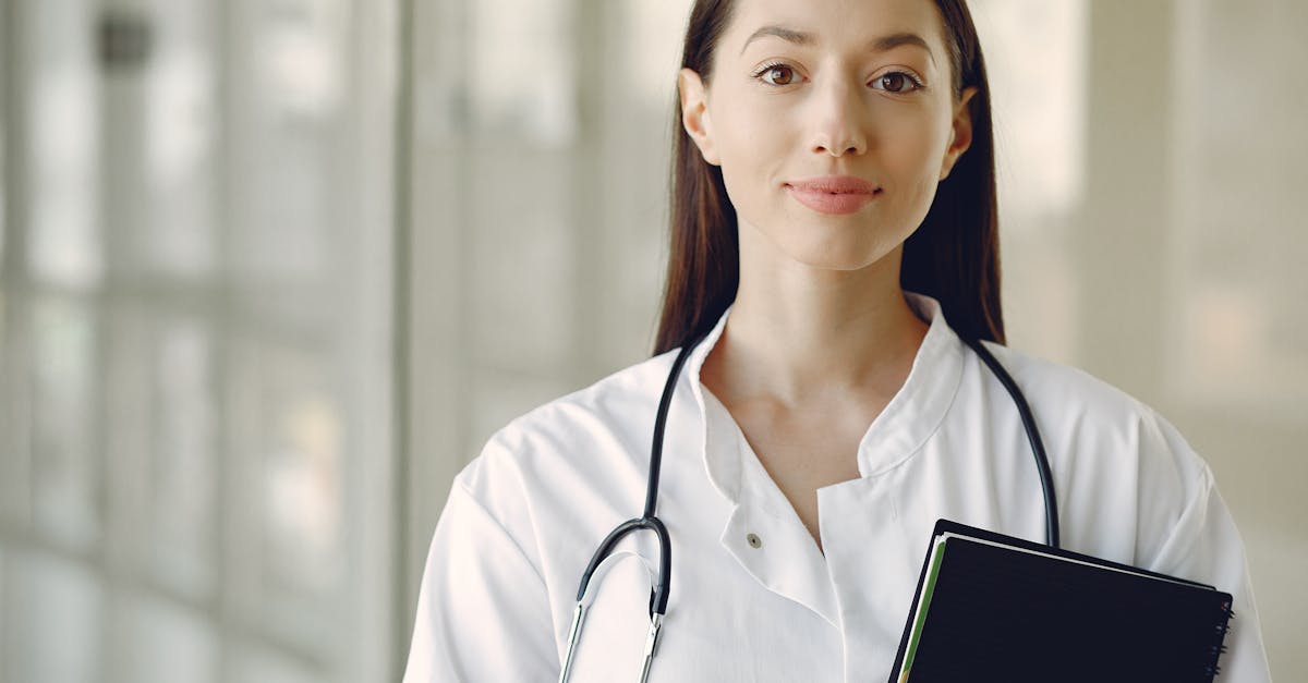 Crop smiling young ethnic female doctor in medical uniform with stethoscope and notebook standing in