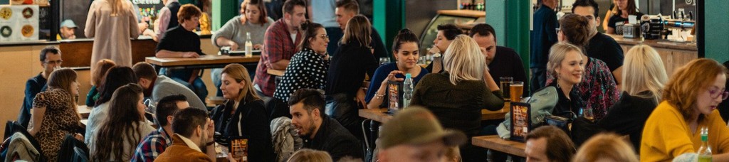 Crowded food hall with diverse people enjoying meals and drinks.