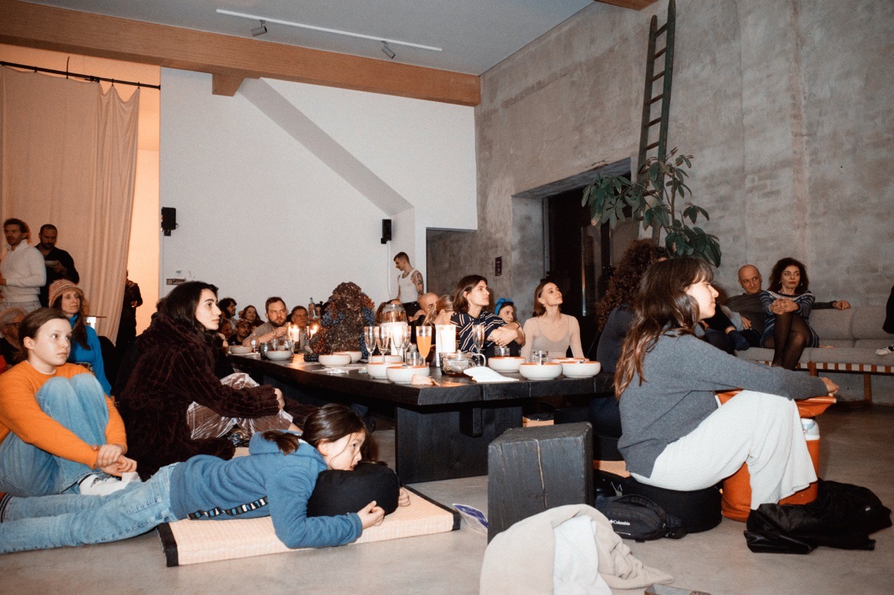 A woman in an orange sweater smiling while looking at a tablet, with a pen in hand.