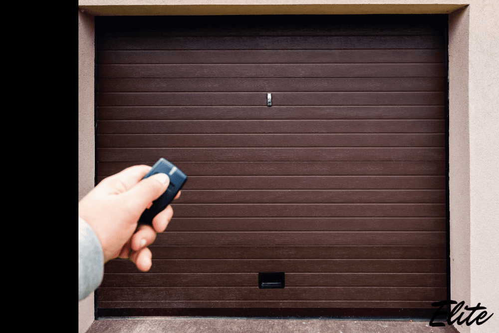 Hand using a remote to open a brown garage door serviced by Elite Garage Door.