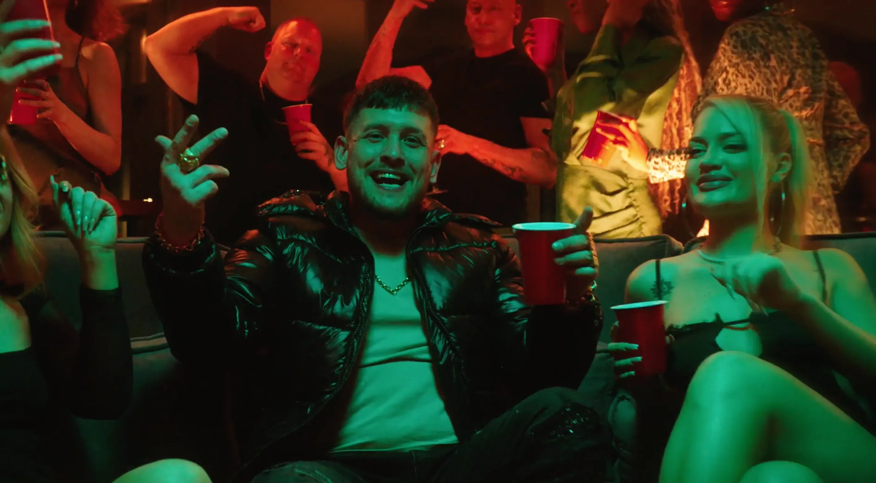 A man in a busy bar with women sat around him holding a drink