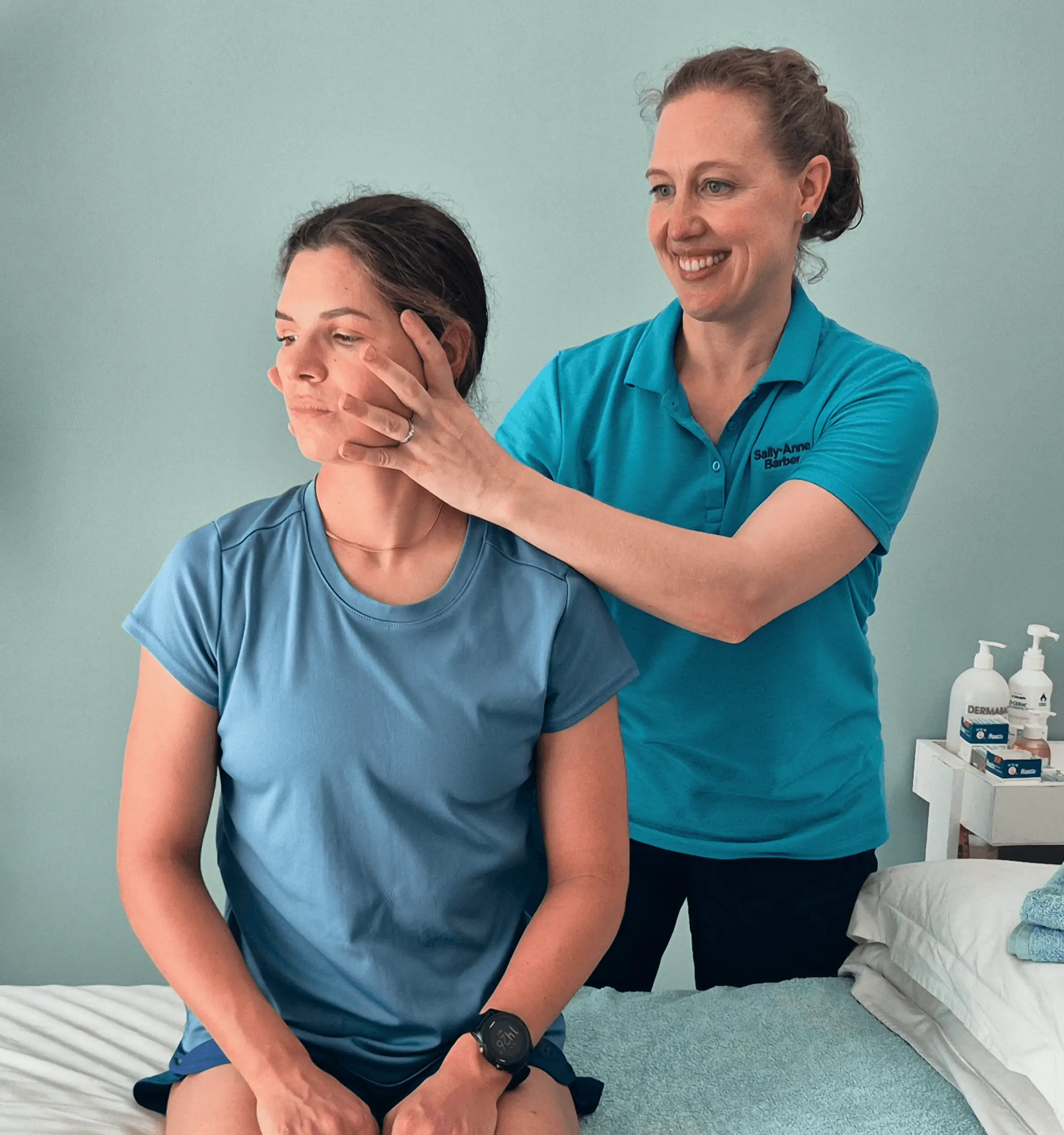 A Physiotherapist performs a C2 rotational SNAG head rotation mobilisation on a seated client for concussion treatment.