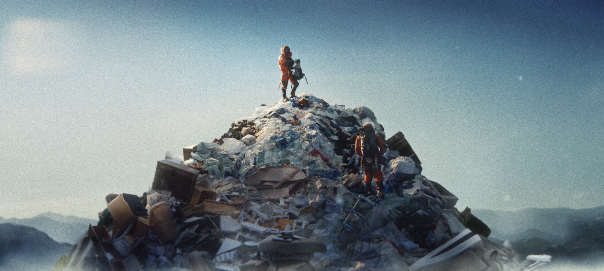 Solitary figure still from The Summit, a climber pulling gear from a pack atop a debris-covered peak.