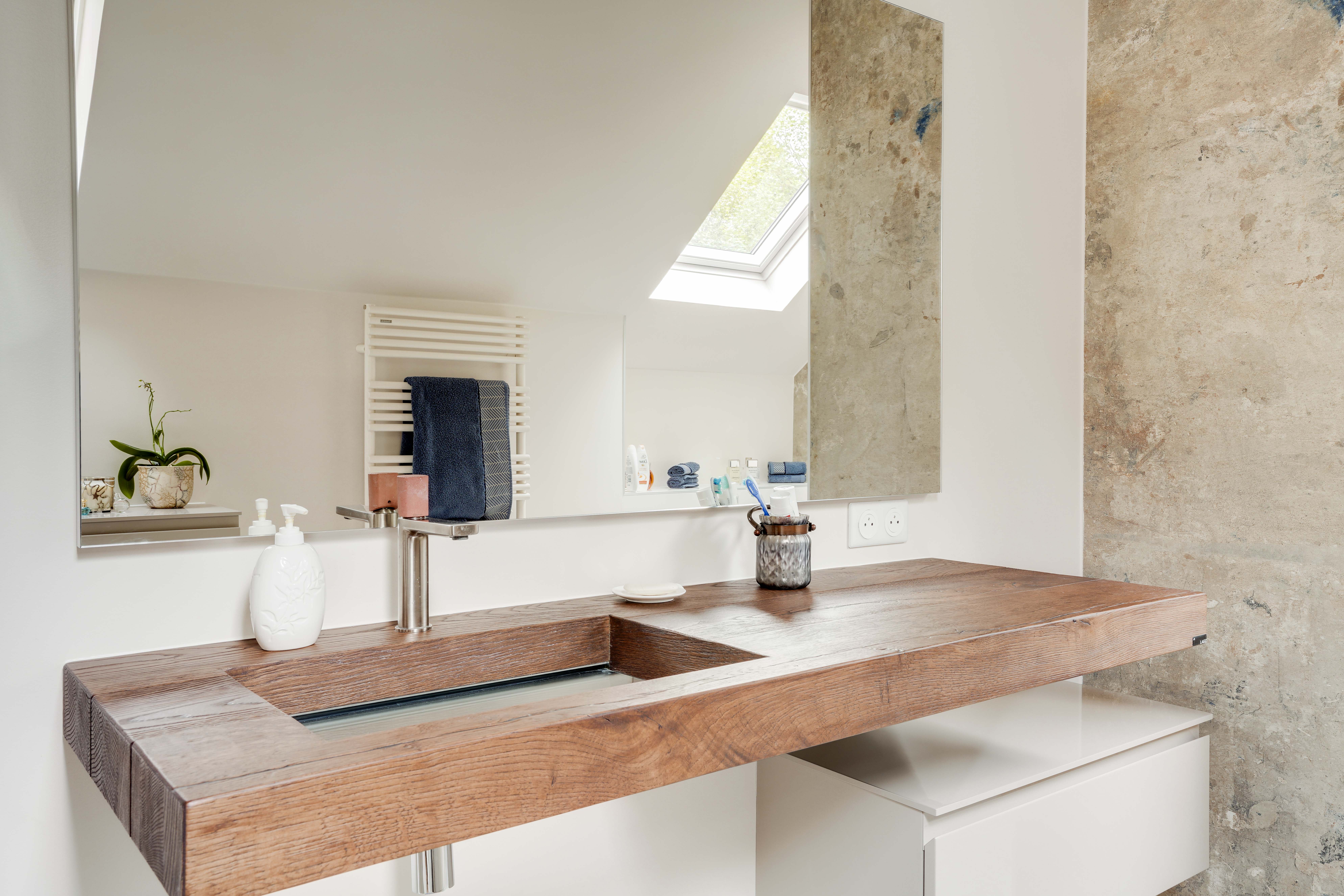 Transformation salle de bains 77 avec lavabo bois, grand miroir, puits de lumière naturelle et murs blancs épurés, rénovation complète.