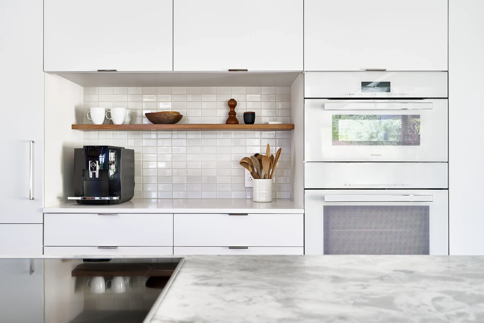 Closeup of the oven wall, highlighting the backsplash and custom white laminate cabinetry, a testament to the Eichler's sophisticated charm. Photo by Todd Huge.