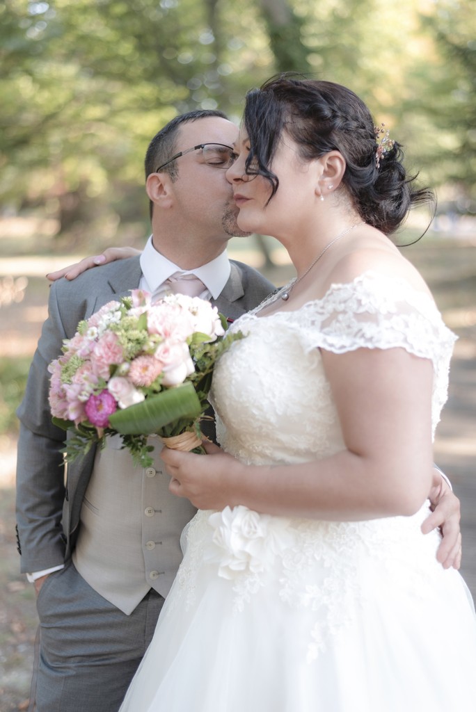 Elegant bride captured from behind holding a delicate bouquet of pastel roses — fine art wedding portrait in a serene garden. Élégante mariée photographiée de dos tenant un bouquet délicat de roses pastel — portrait de mariage artistique dans un jardin paisible.