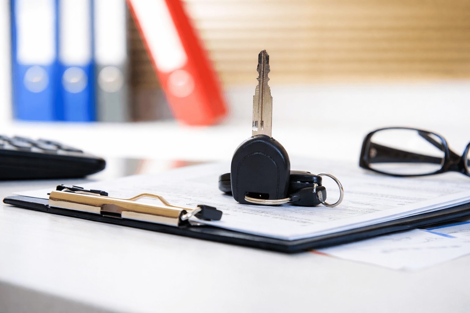 Car keys standing on a clipboard with documents on a desk.