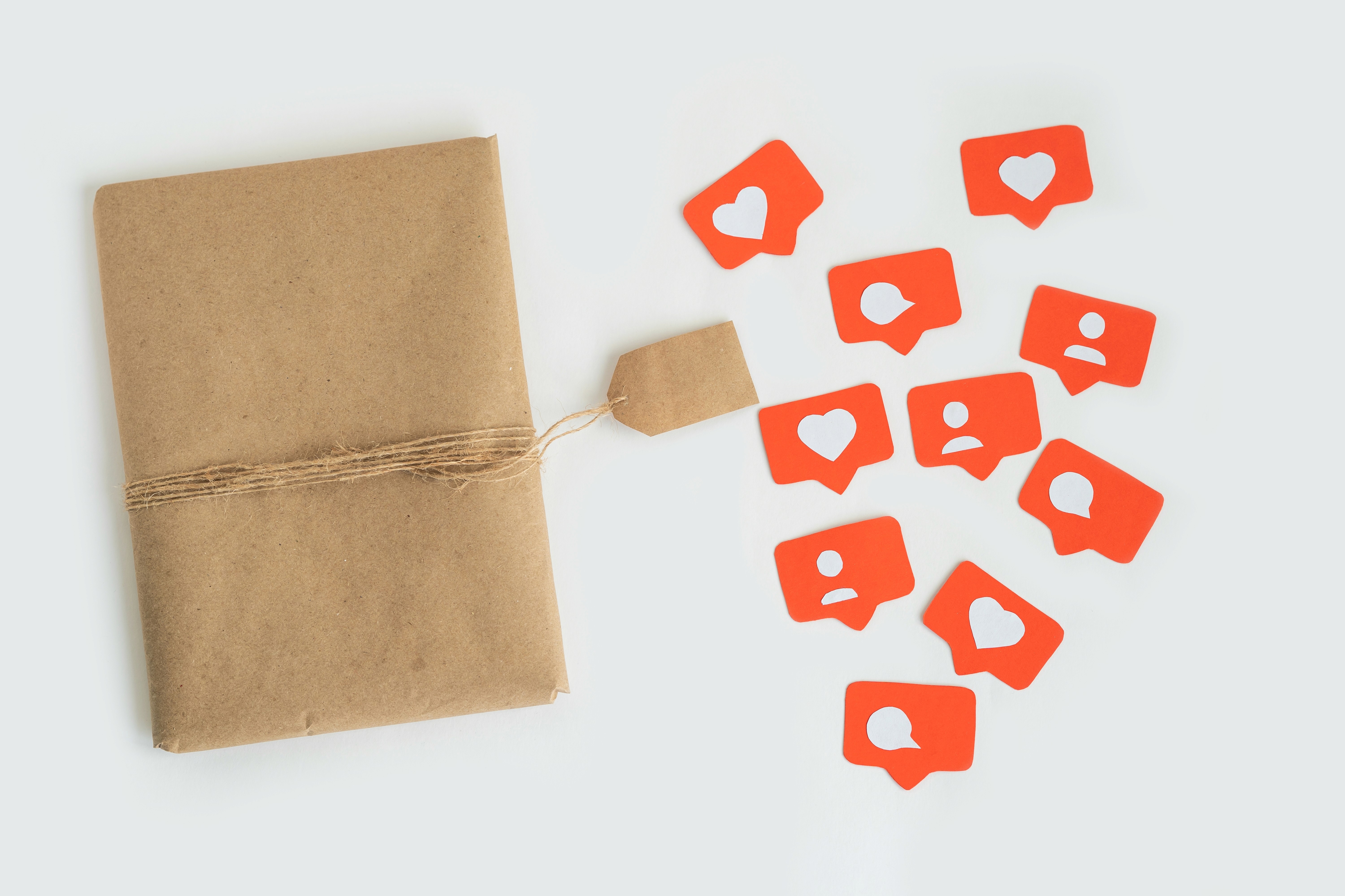 A brown paper wrapped package with a gift tag next to scattered red social media notification icons including hearts follows and comments, representing how genuinely valuable content earns engagement and builds audience trust organically