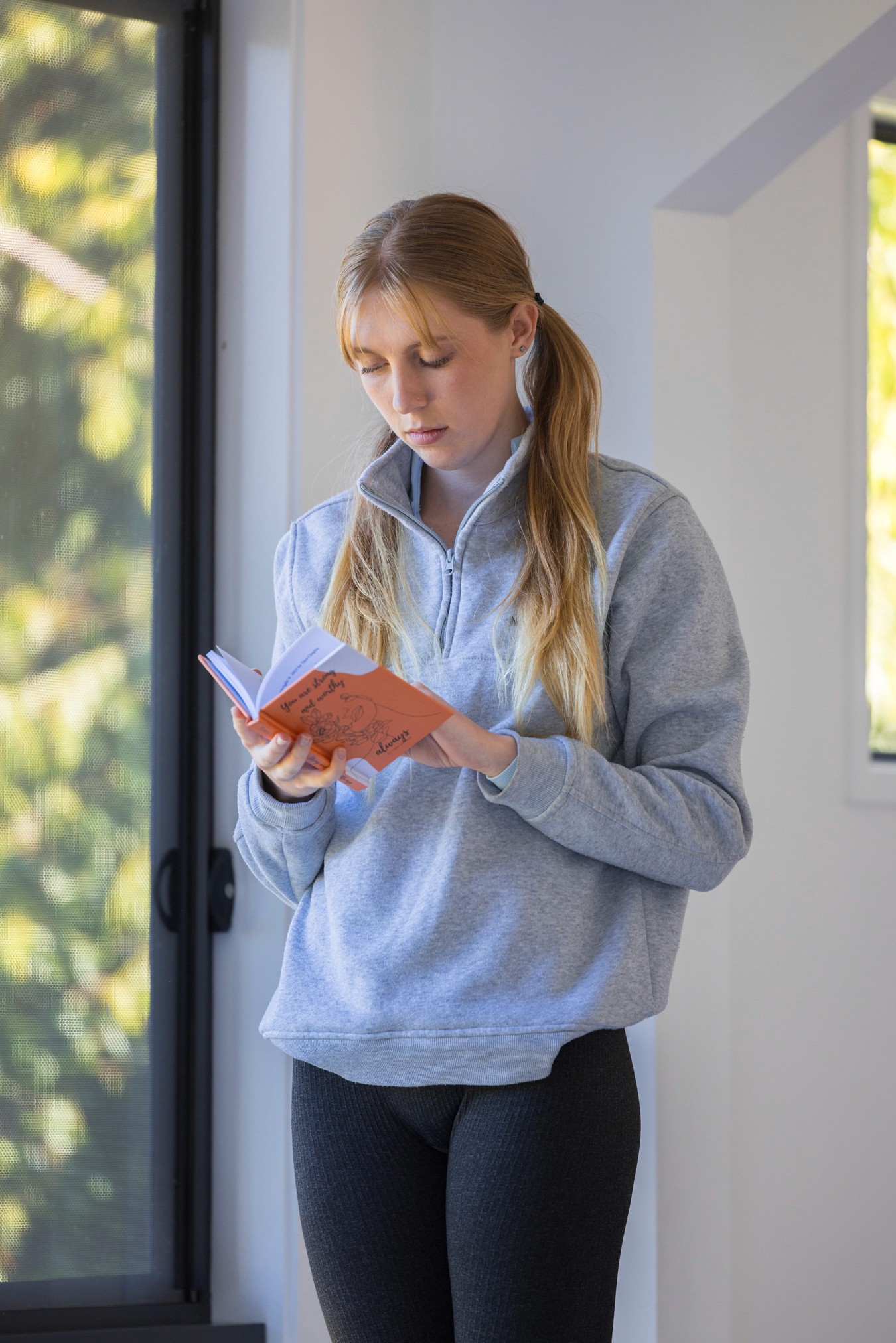Young woman standing, reading from an orange book