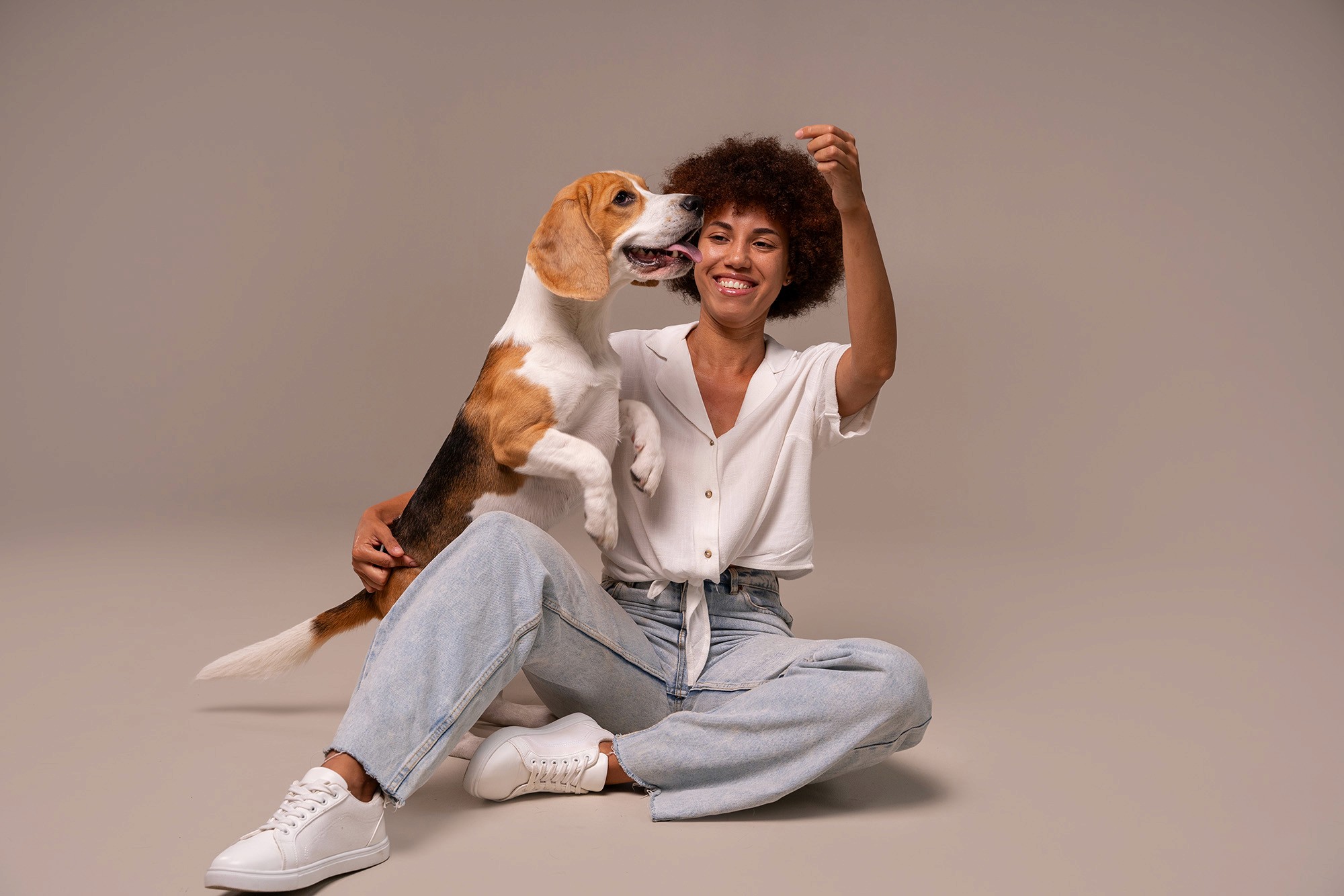 Woman sitting on the floor in a studio, smiling and playing with her happy Beagle