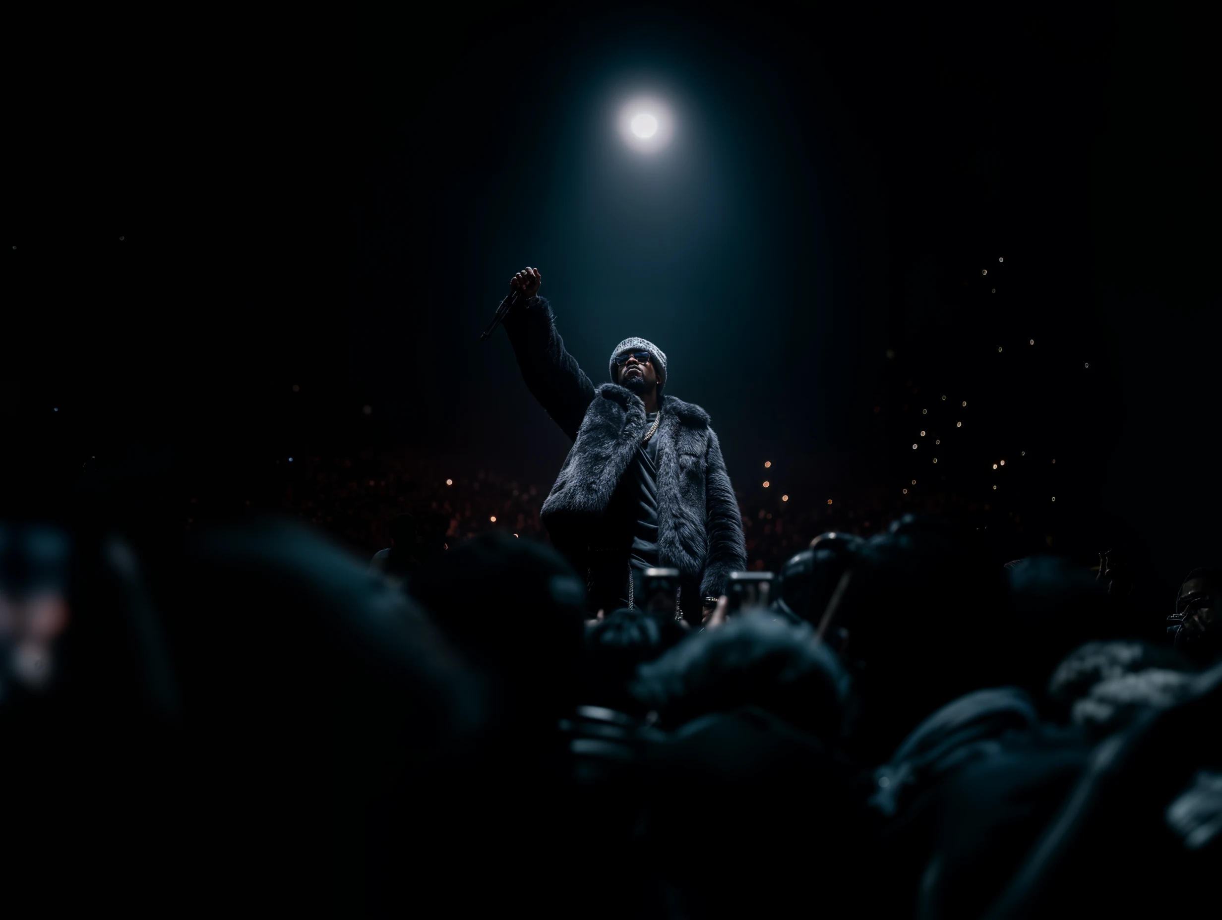Hip hop artist performing on stage under a spotlight in front of a crowd