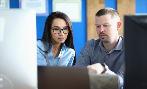A woman with glasses and a man looking intently at a laptop computer together in an office setting