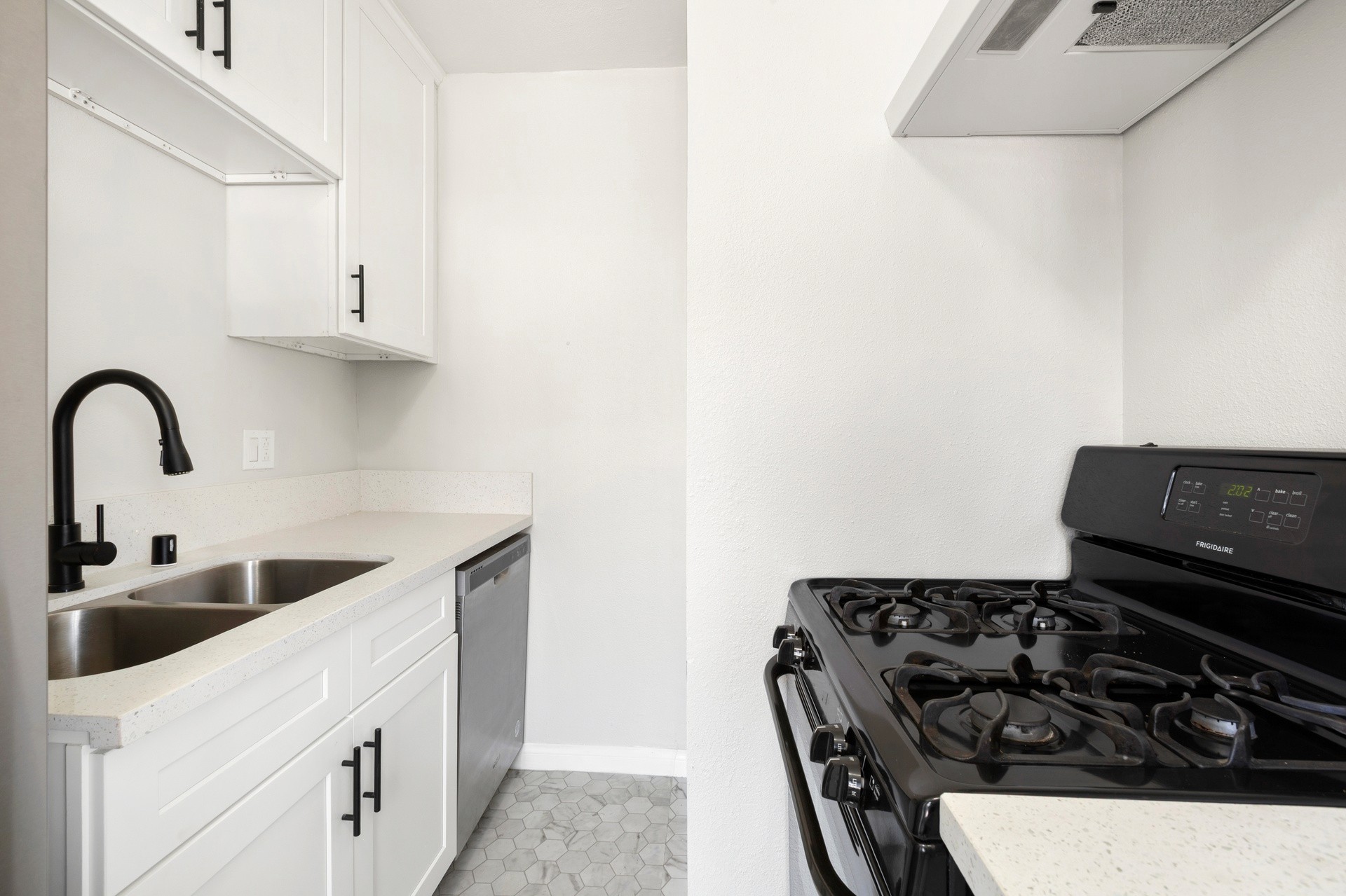 A modern, minimalistic kitchen at 4421 Wall, featuring white cabinetry, a stainless steel sink, and a black stove.