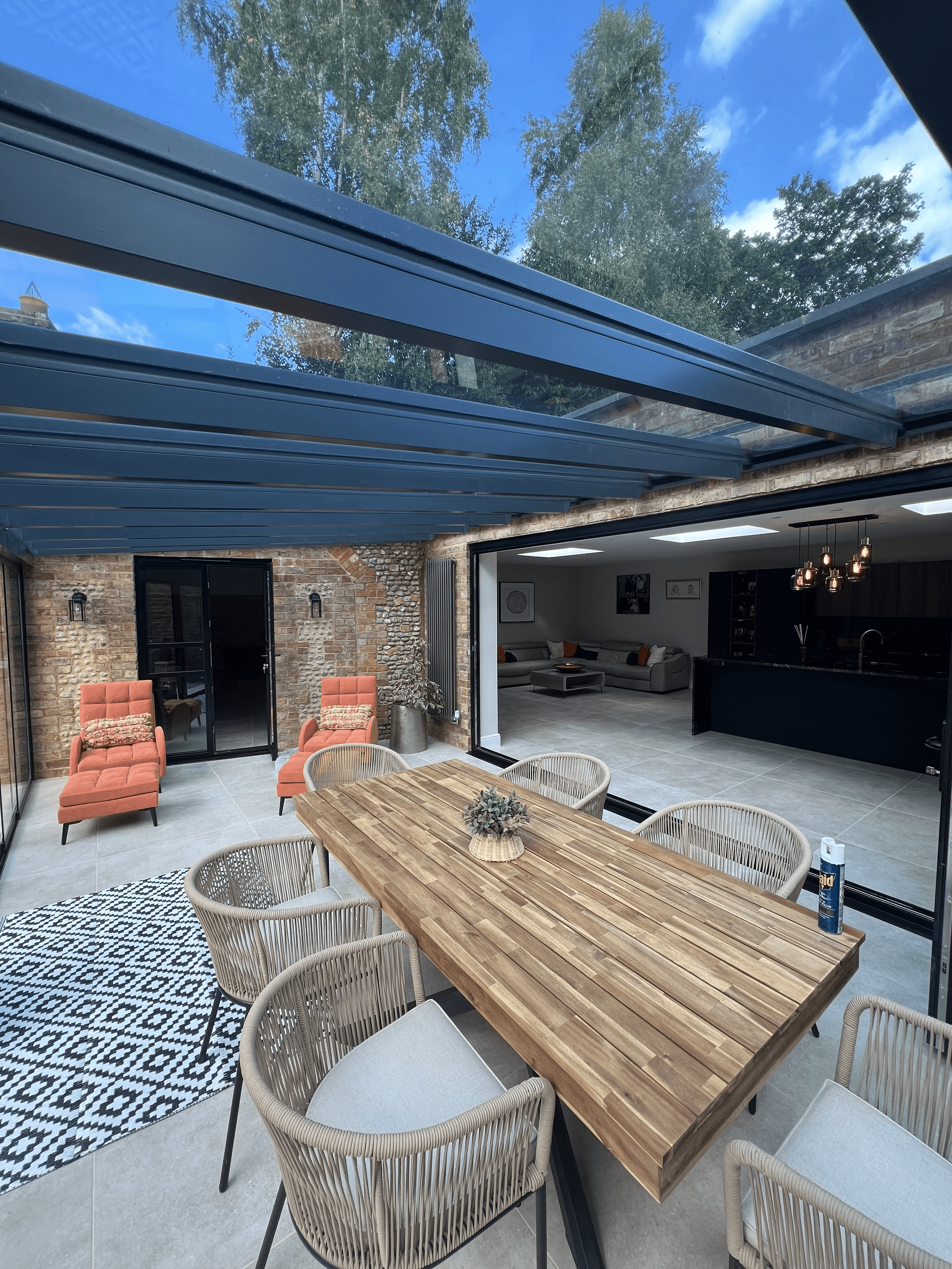 Contemporary glass-roof extension with exposed brick walls, featuring a wooden dining set and outdoor seating, completed by PPM Builders.