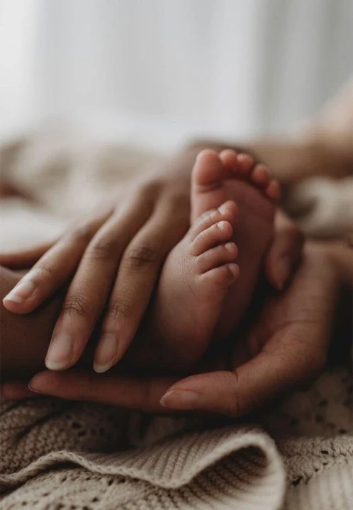Newborn feet resting beneath an adult hand