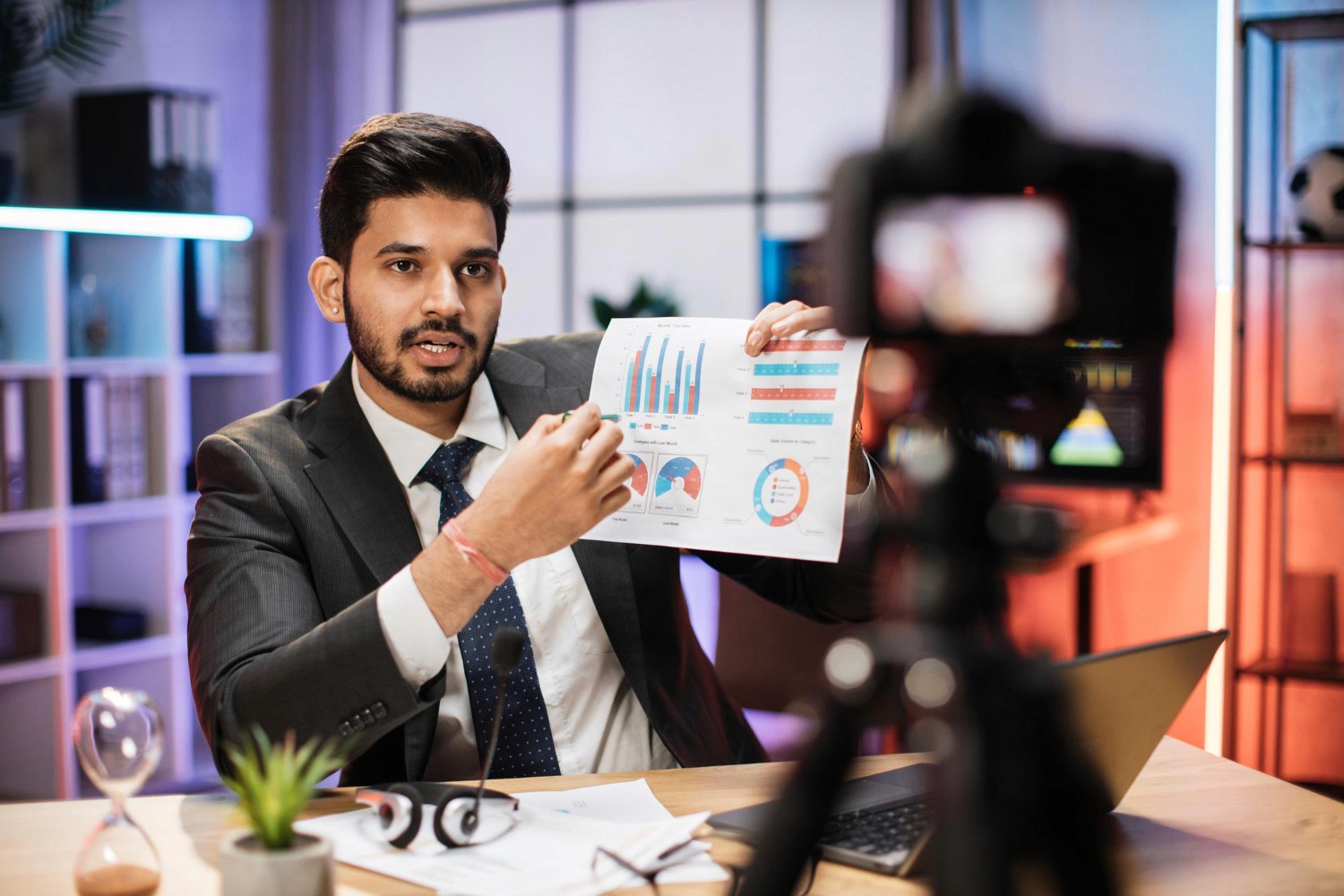 A man in a suit stands by a table, holding a chart, engaged in a professional discussion.