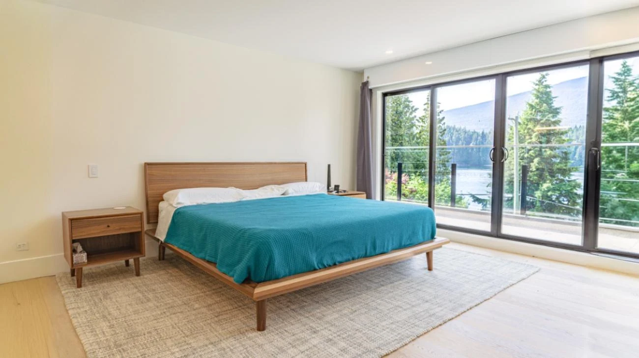 Master bedroom with minimalist design, platform bed, and floor-to-ceiling glass doors opening to private deck with mountain views in Vancouver