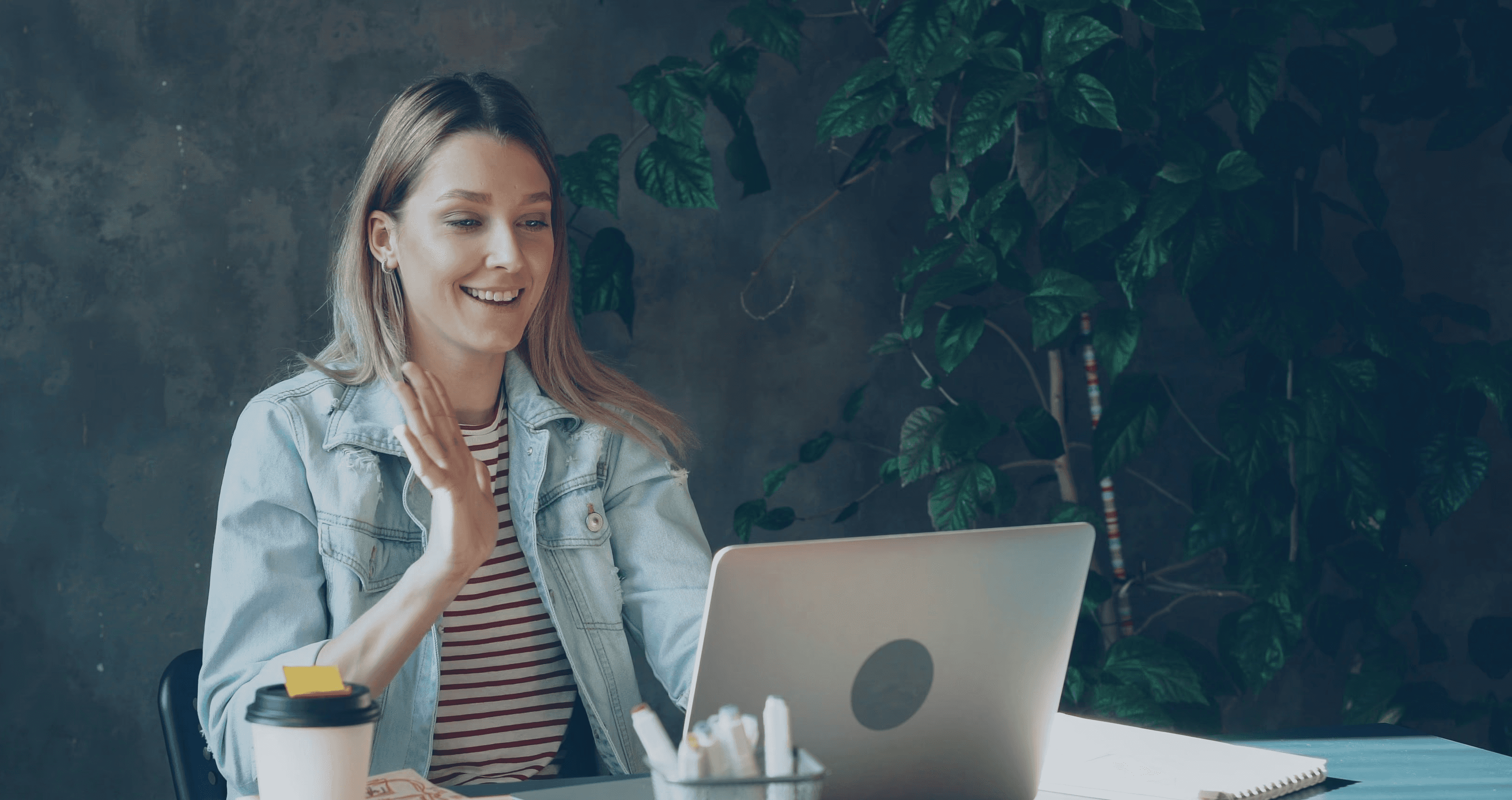 Woman waving during a video call on her laptop.