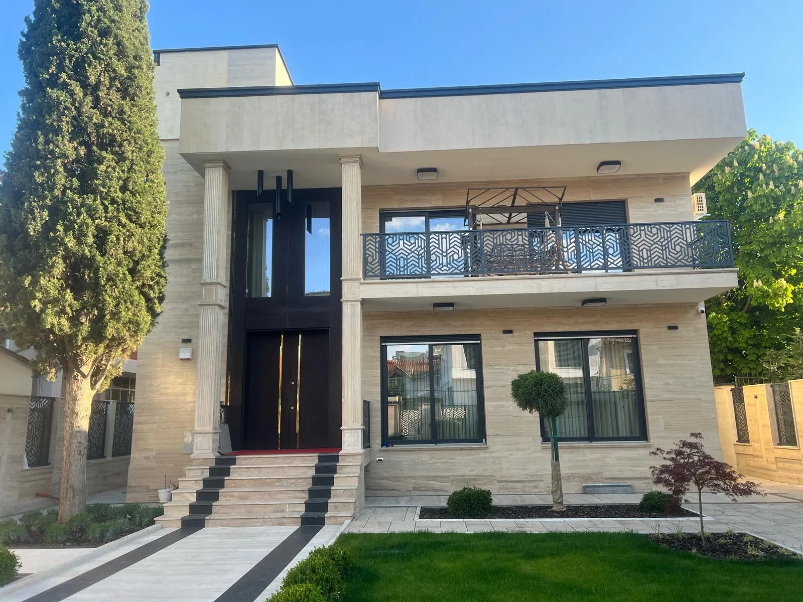 Modern private residence in Skopje with stone cladding, tall columns, and landscaped front garden. Terraplan Partners provided architectural planning and supervision.