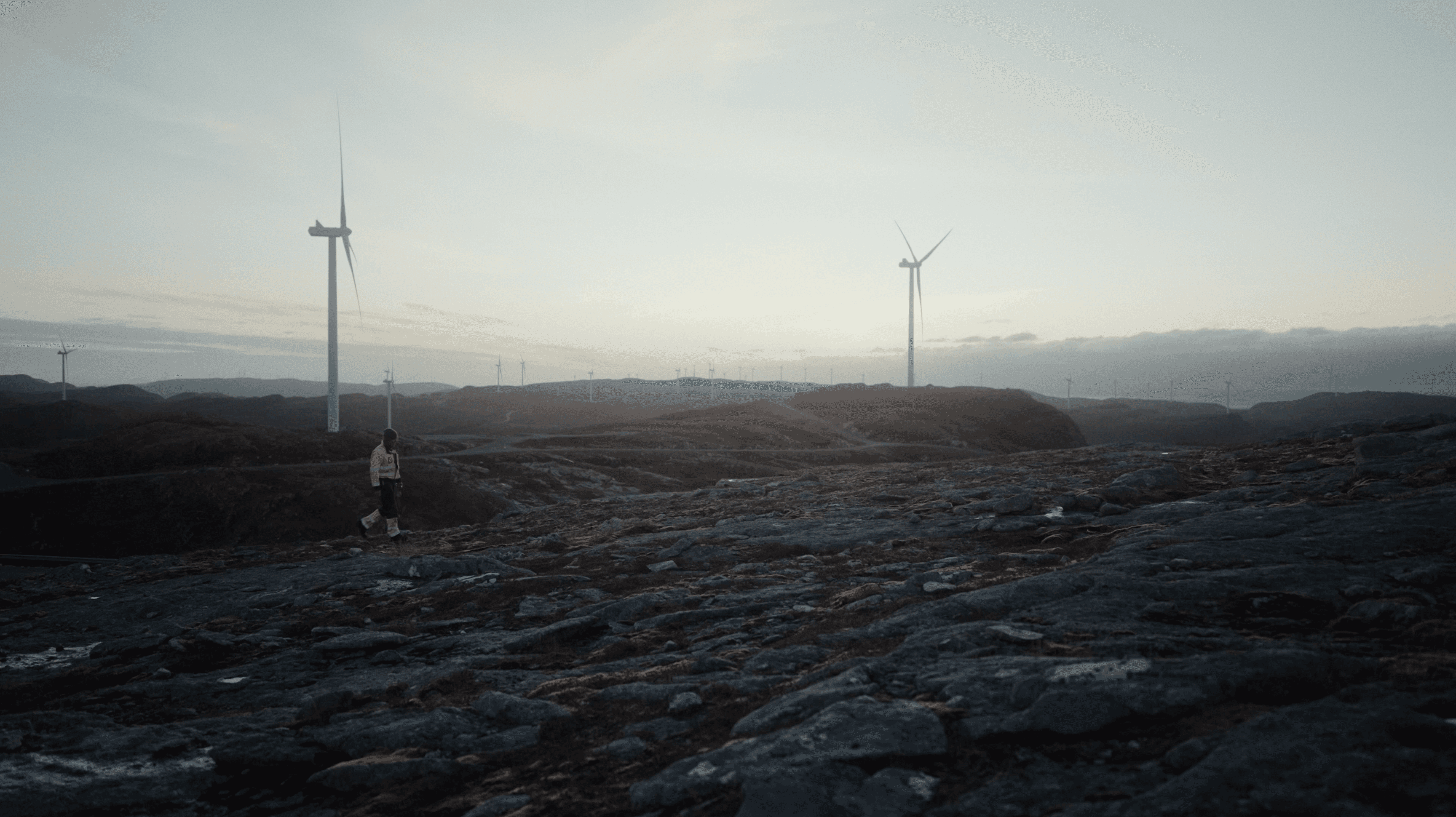 Vindtekniker som går i forgrunnen av en stor vindpark i solnedgang