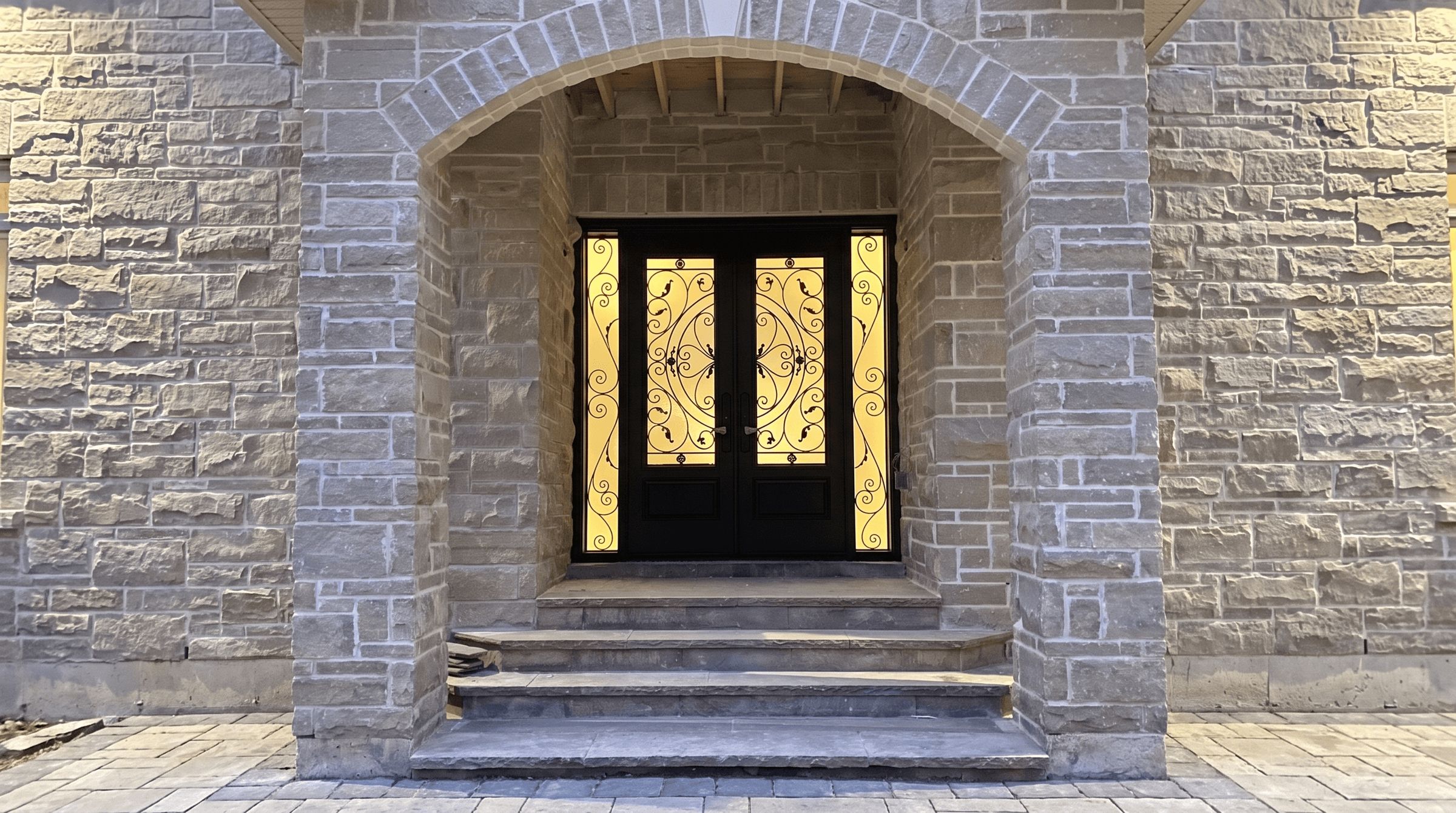 Wrought iron glass double entry door with sidelites glowing at dusk under a stone archway in the Greater Toronto Area