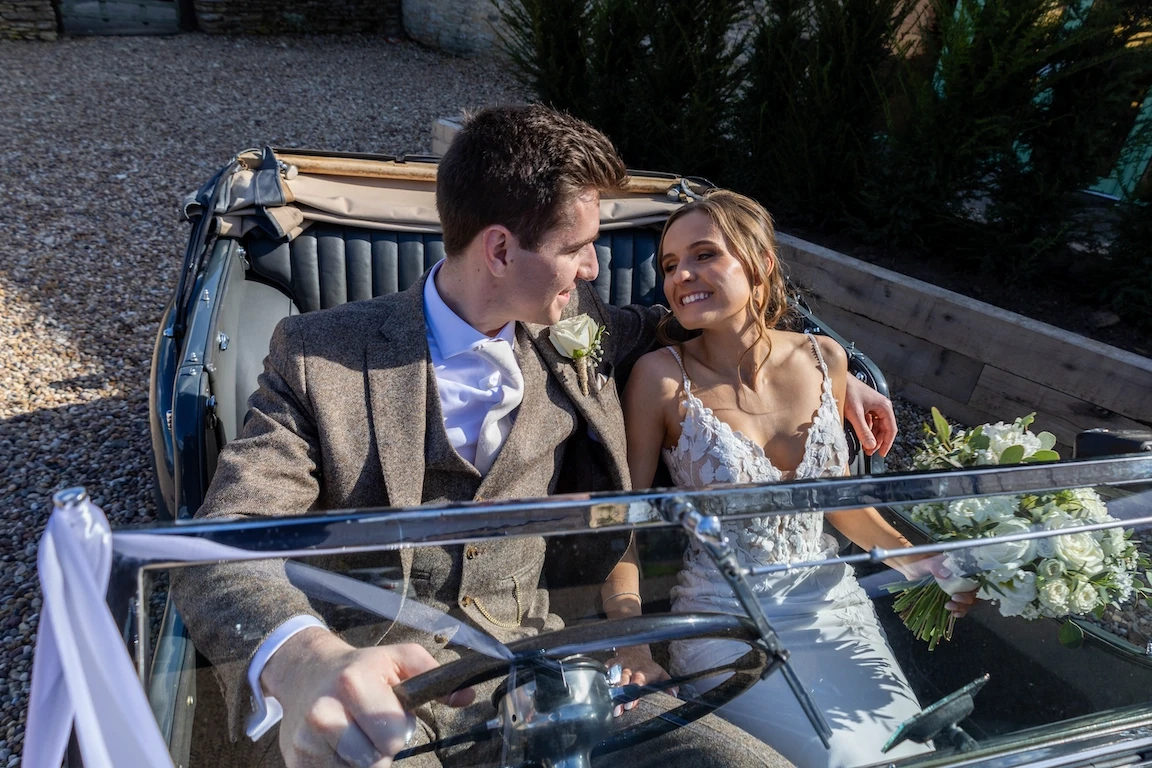 Bride and groom sitting together in a vintage car during their wedding day