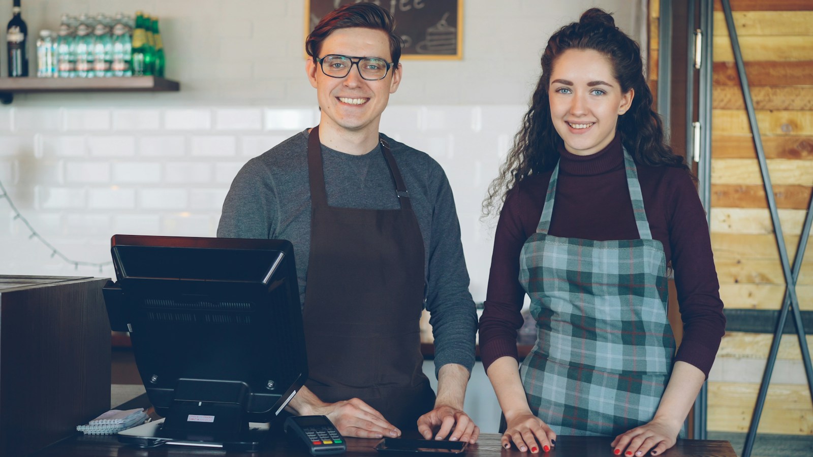 Two smiling cafe workers stand behind a counter