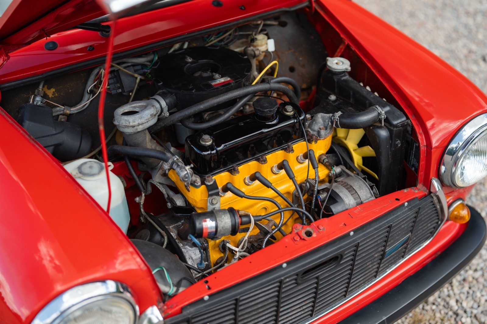 A close-up view of a red car's engine bay, showcasing a black engine with yellow accents and various components.